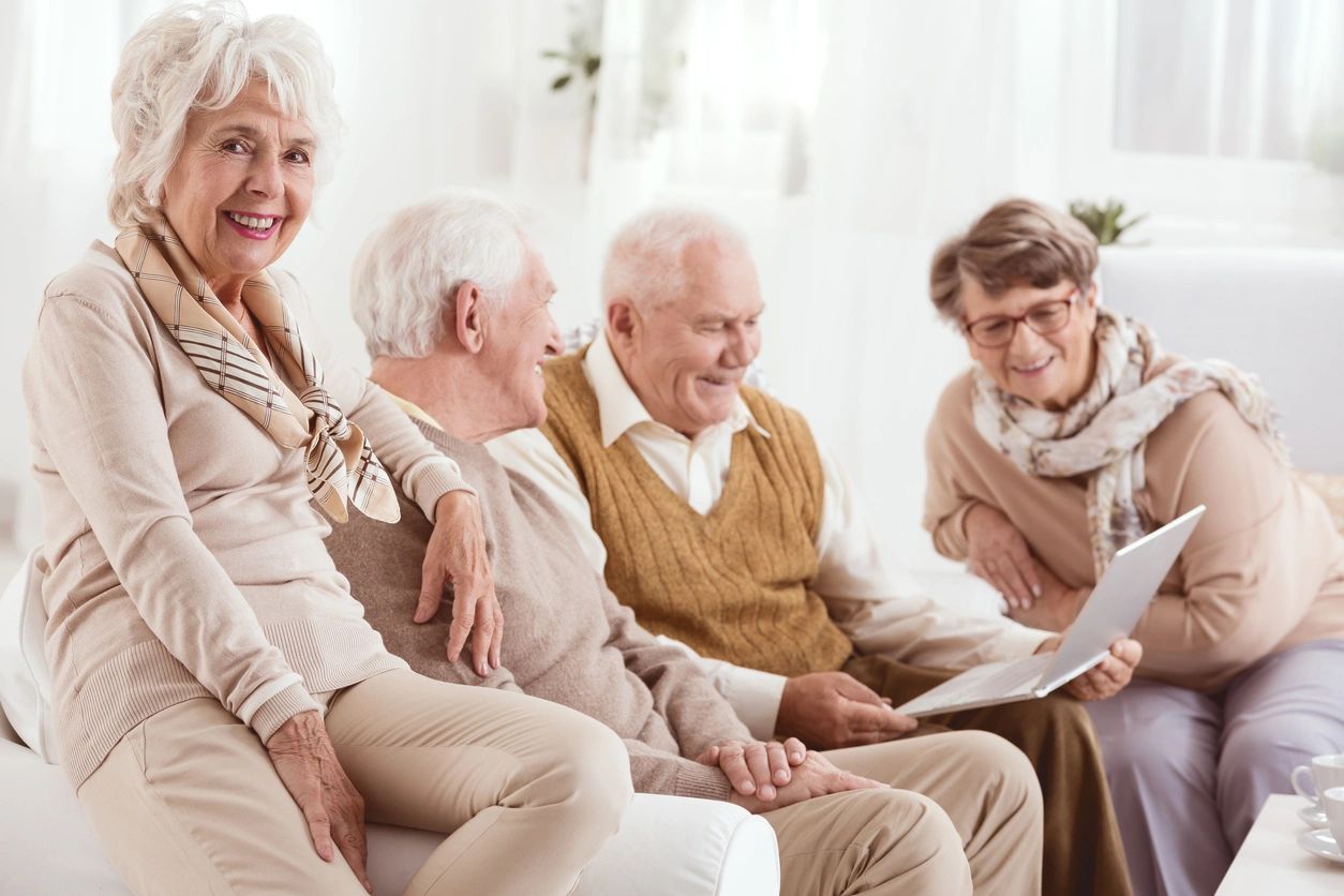 Elderly friends looking at laptop on computer while sitting on couch.