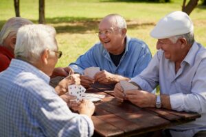 elderly friends playing cards at table outdoors